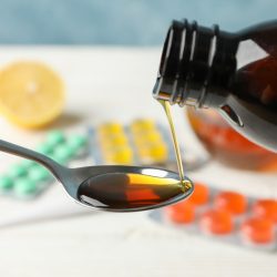 Syrup pouring into a spoon against pill background, close up